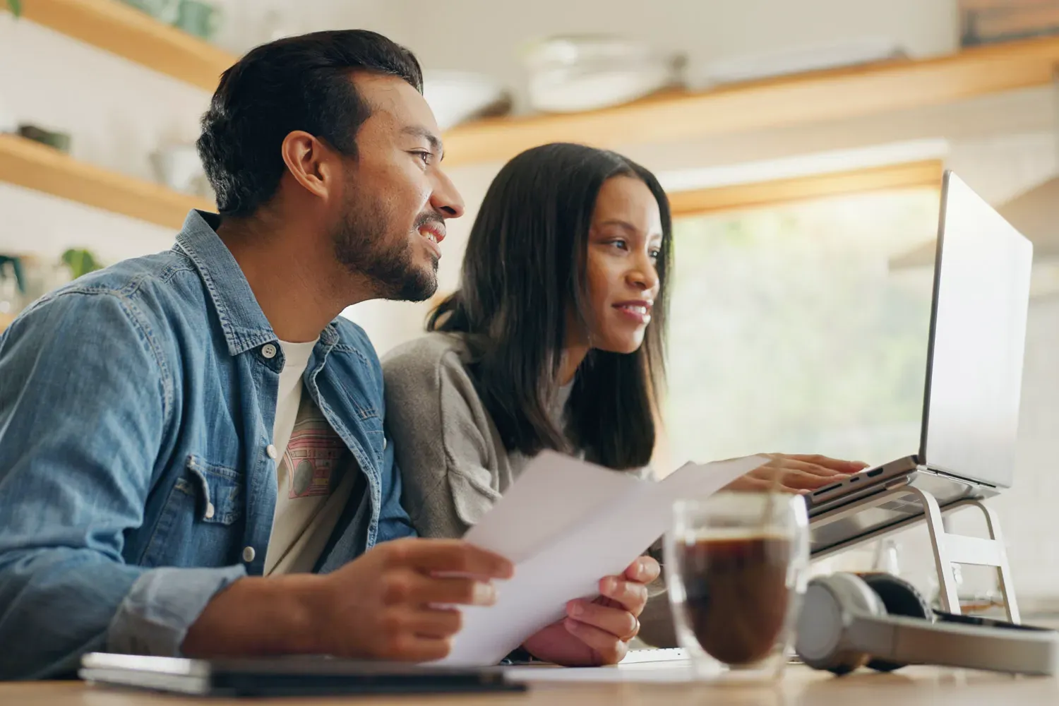 Smiling couple sitting at a desk with papers and a laptop, reviewing tips for maintaining credit card safety and protecting financial information online.