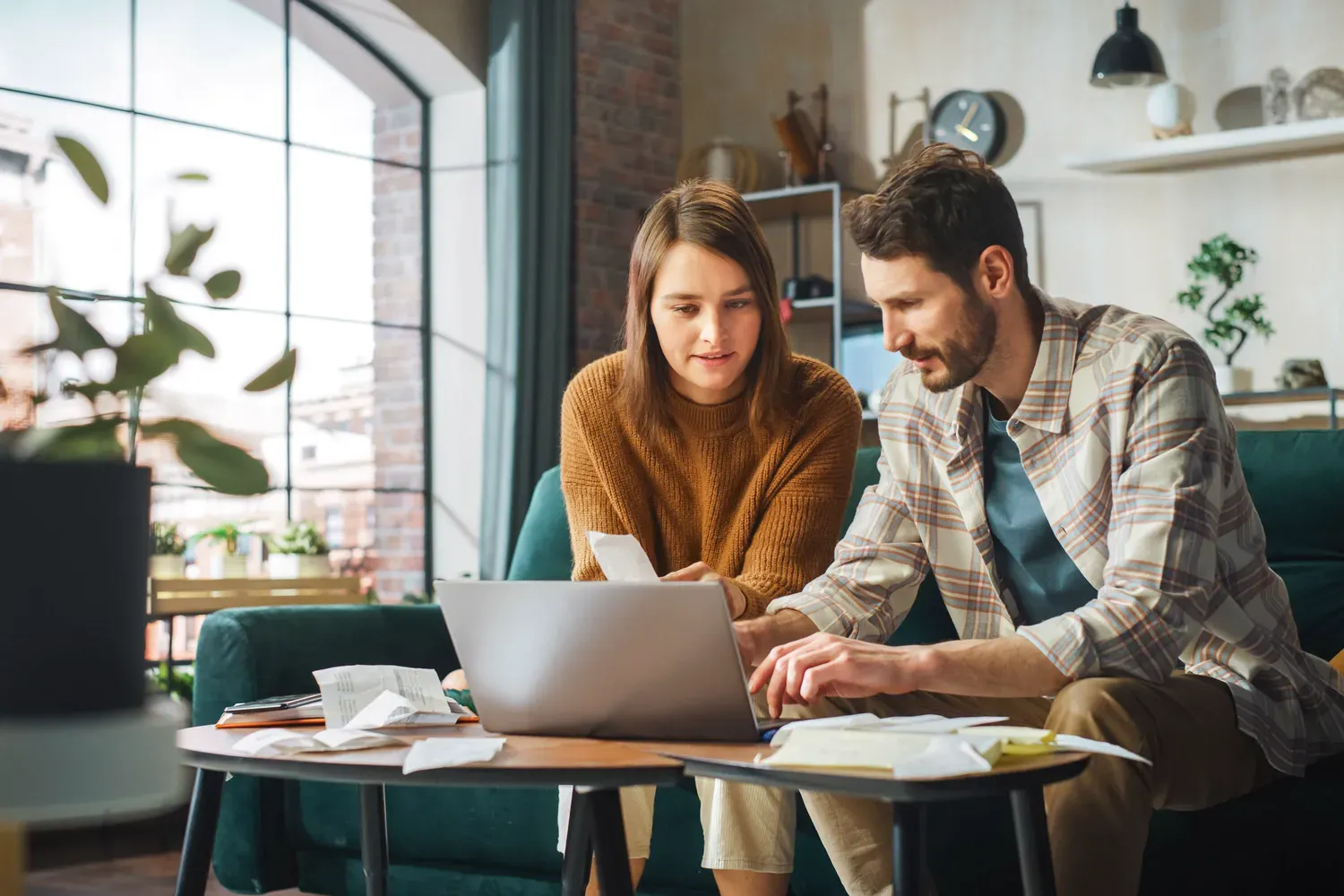 Couple sitting at home reviewing receipts and budgeting on a laptop, representing practical ways to save money on everyday expenses.
