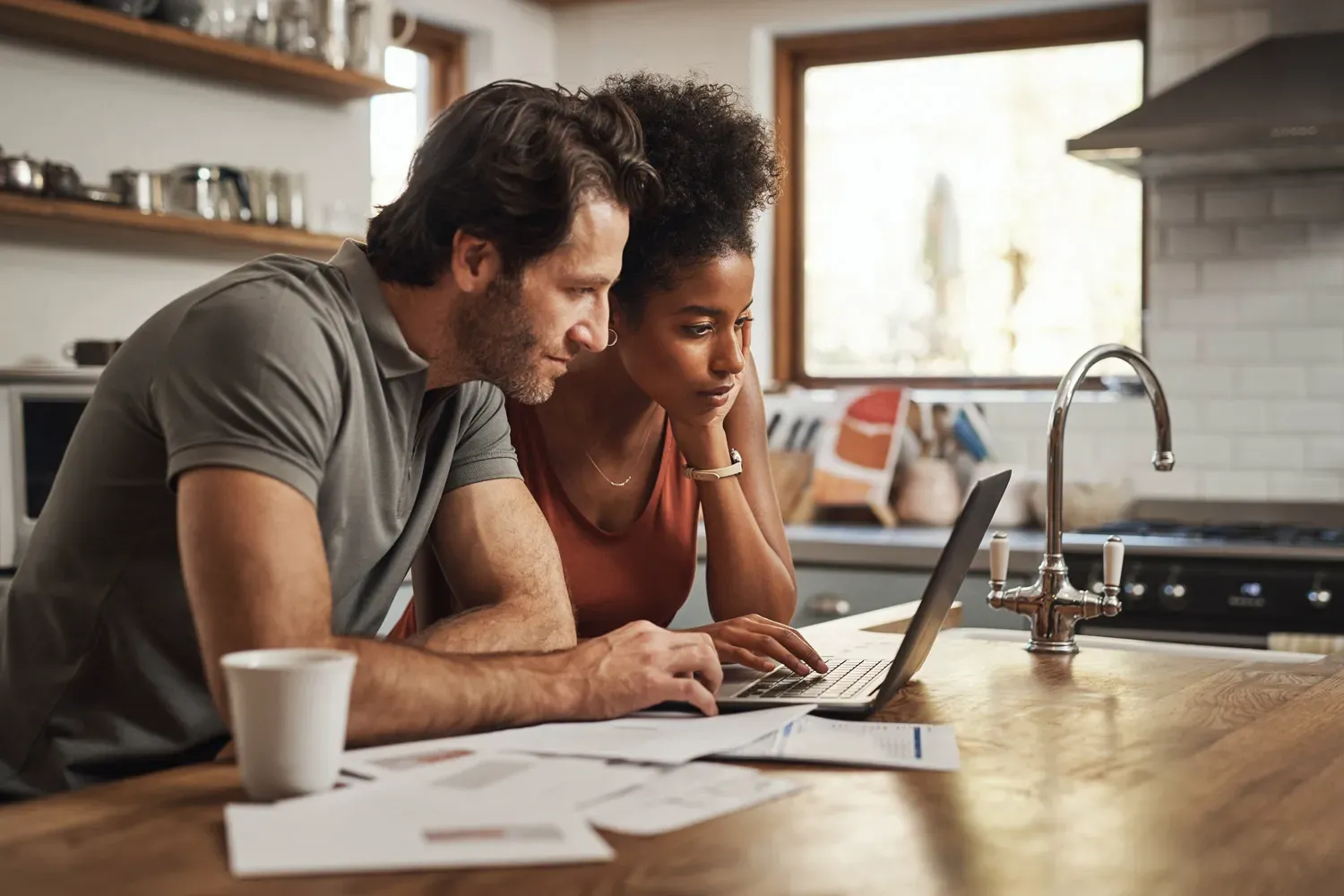 Couple reviewing financial documents and using a laptop together at a kitchen counter to plan for retirement savings.