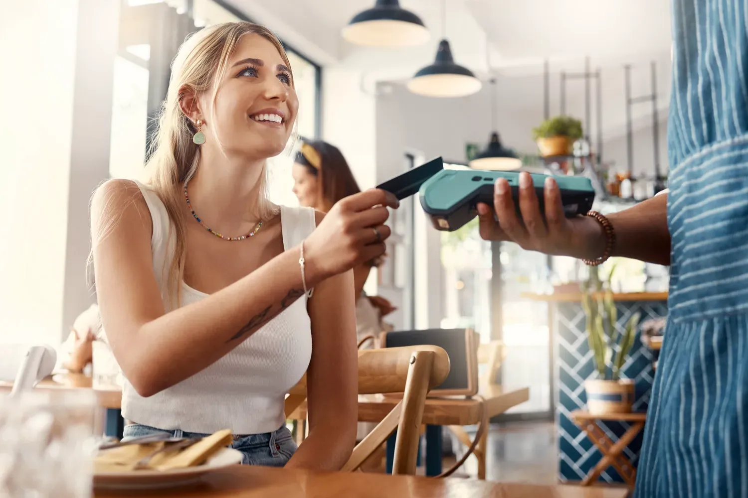 Smiling woman in a restaurant uses her credit card to make a payment, illustrating different types of credit cards and their everyday uses.