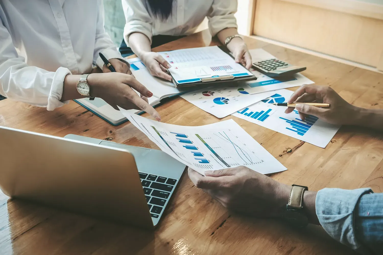 Group of people reviewing charts and financial reports at a wooden table, discussing different types of traditional investments.
