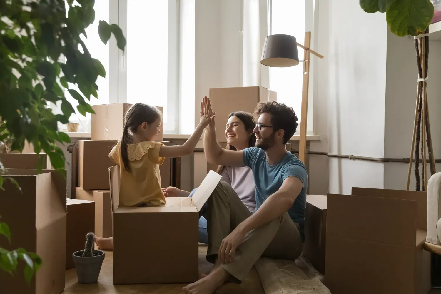 Happy family sitting among moving boxes in their new home, celebrating with a high-five to represent achieving homeownership through different types of mortgages.
