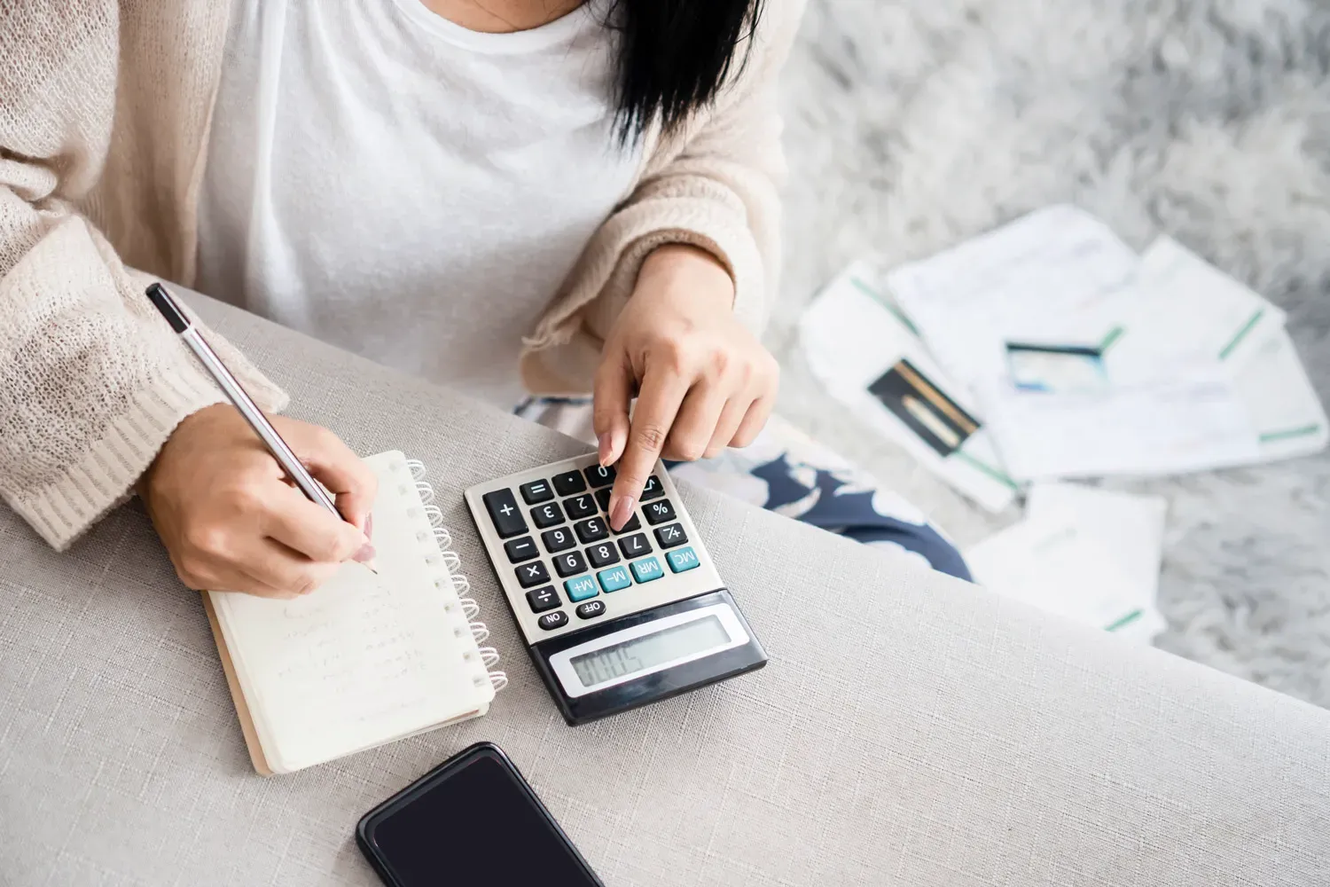 Person using a calculator and writing in a notebook while managing bills, representing the basics of personal finance and budgeting for beginners.