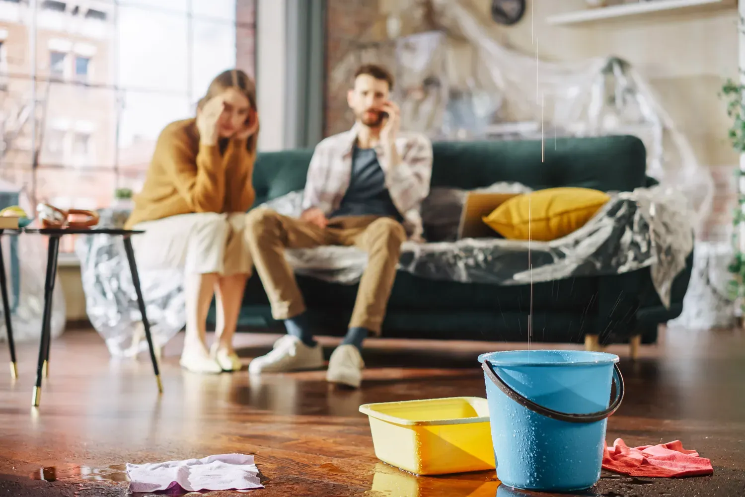 Couple sitting on their couch worried as water leaks from the ceiling into buckets, illustrating the importance of having the right homeowners insurance.