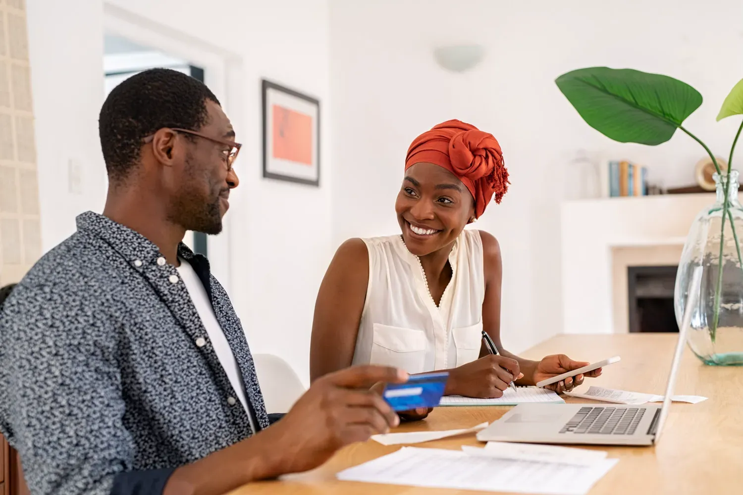 Smiling couple sitting at a table with a laptop and paperwork, discussing how credit cards work and how to use them responsibly.