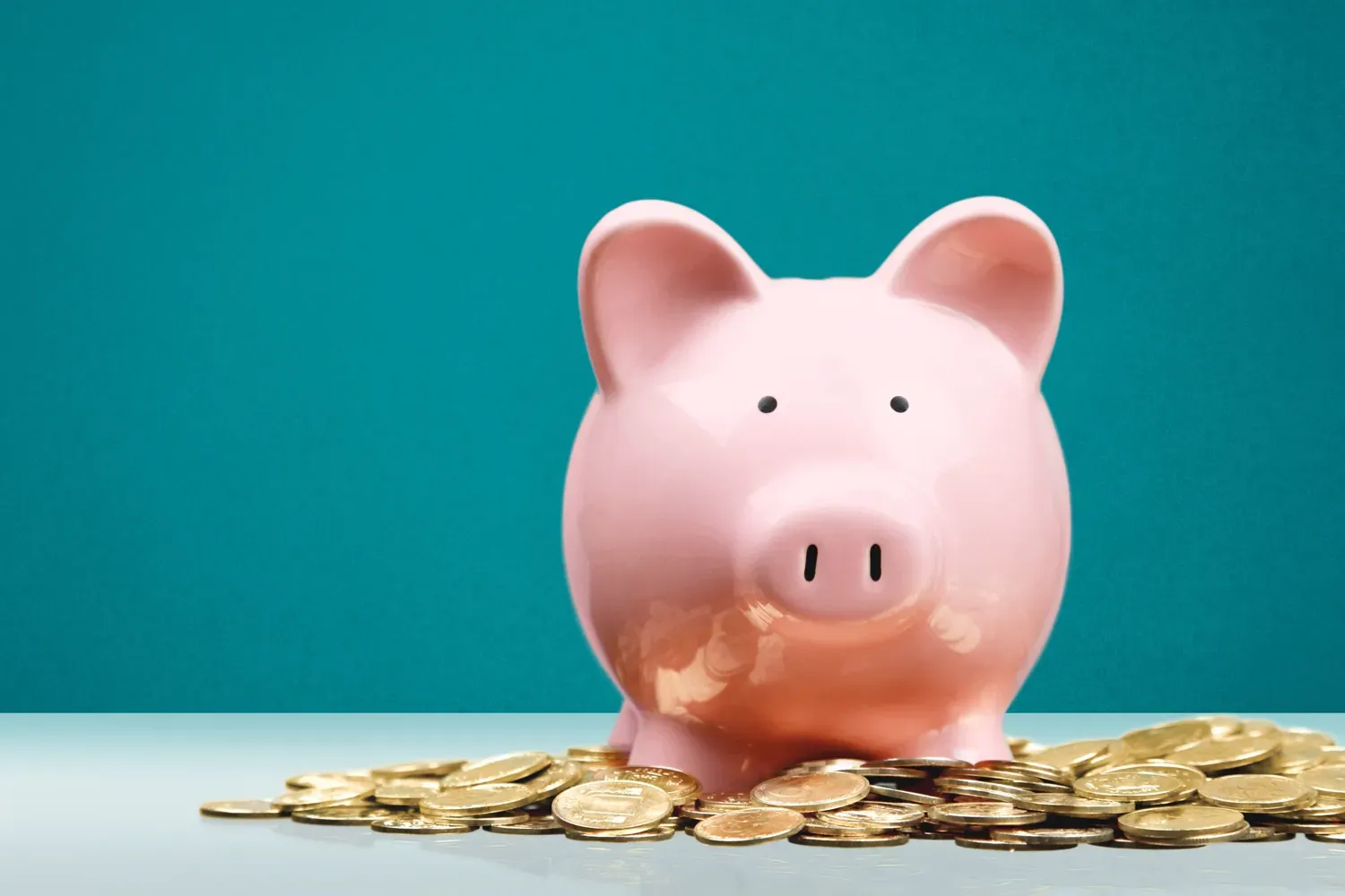 Pink piggy bank sitting on a pile of gold coins against a teal background, symbolizing choosing the right savings account to grow your money.