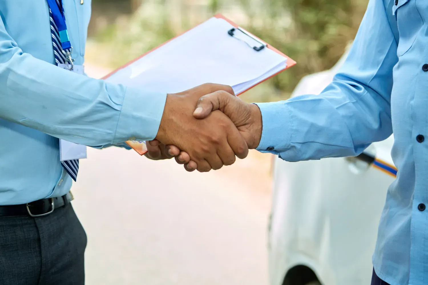 Two people shaking hands outdoors near a car, symbolizing trust and caution in avoiding common car-buying scams.