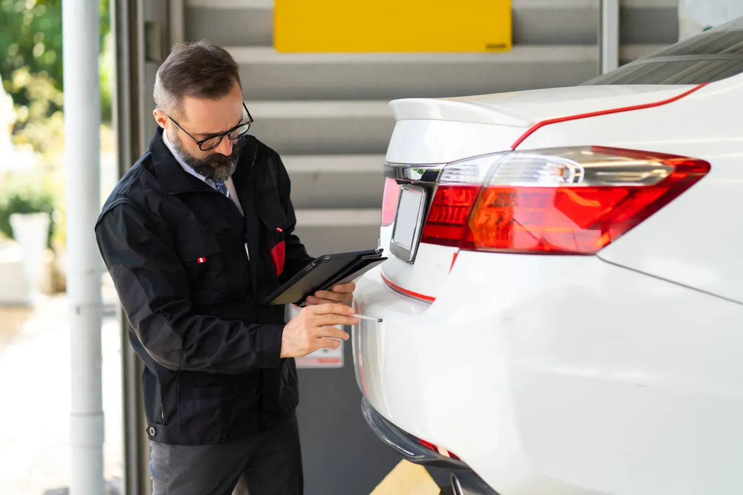 Insurance agent inspecting a car and taking notes on a tablet, representing the process of choosing the best car insurance coverage.