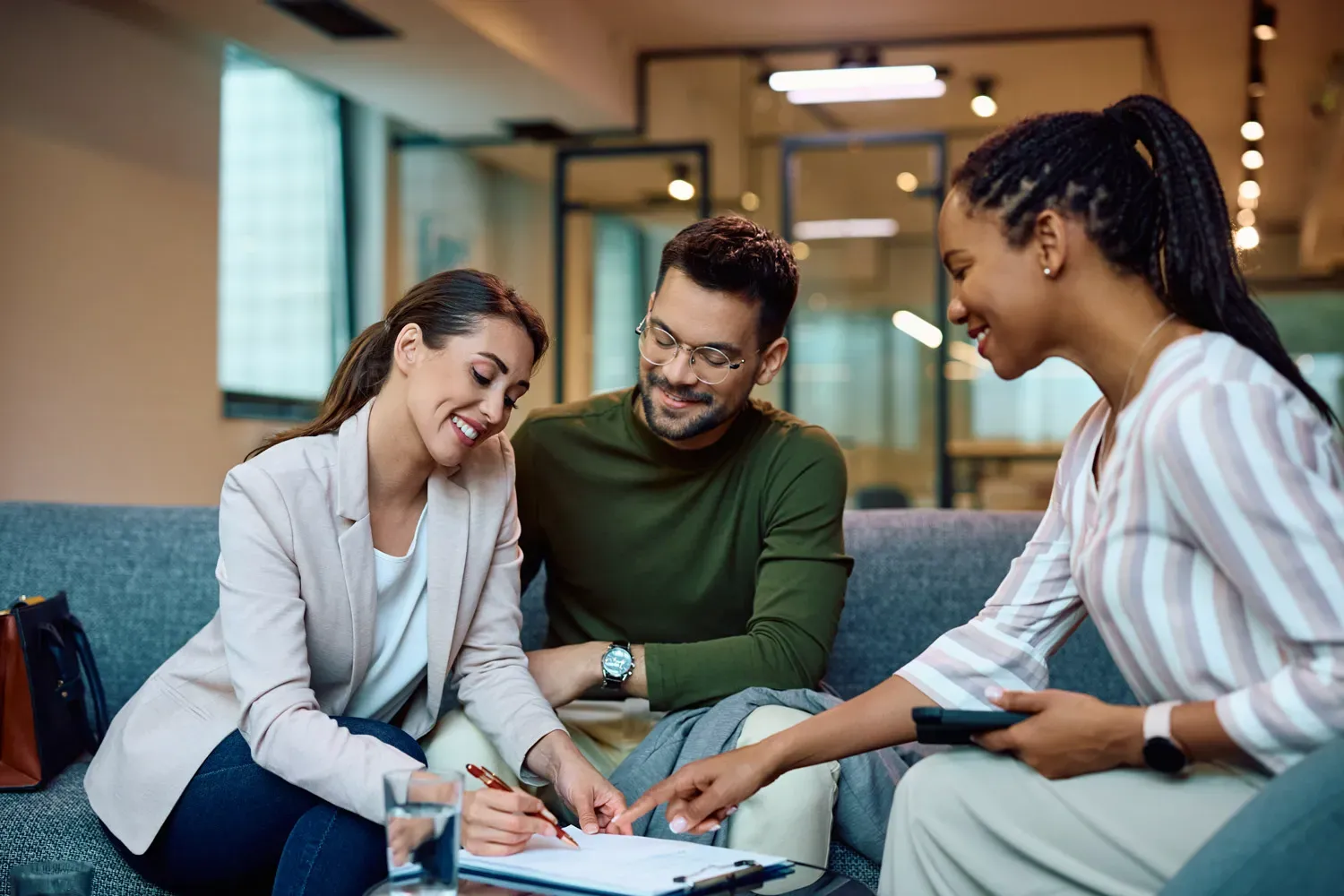 Smiling couple meeting with a financial advisor and signing paperwork, representing how to choose the right lender for a car loan with favorable terms.