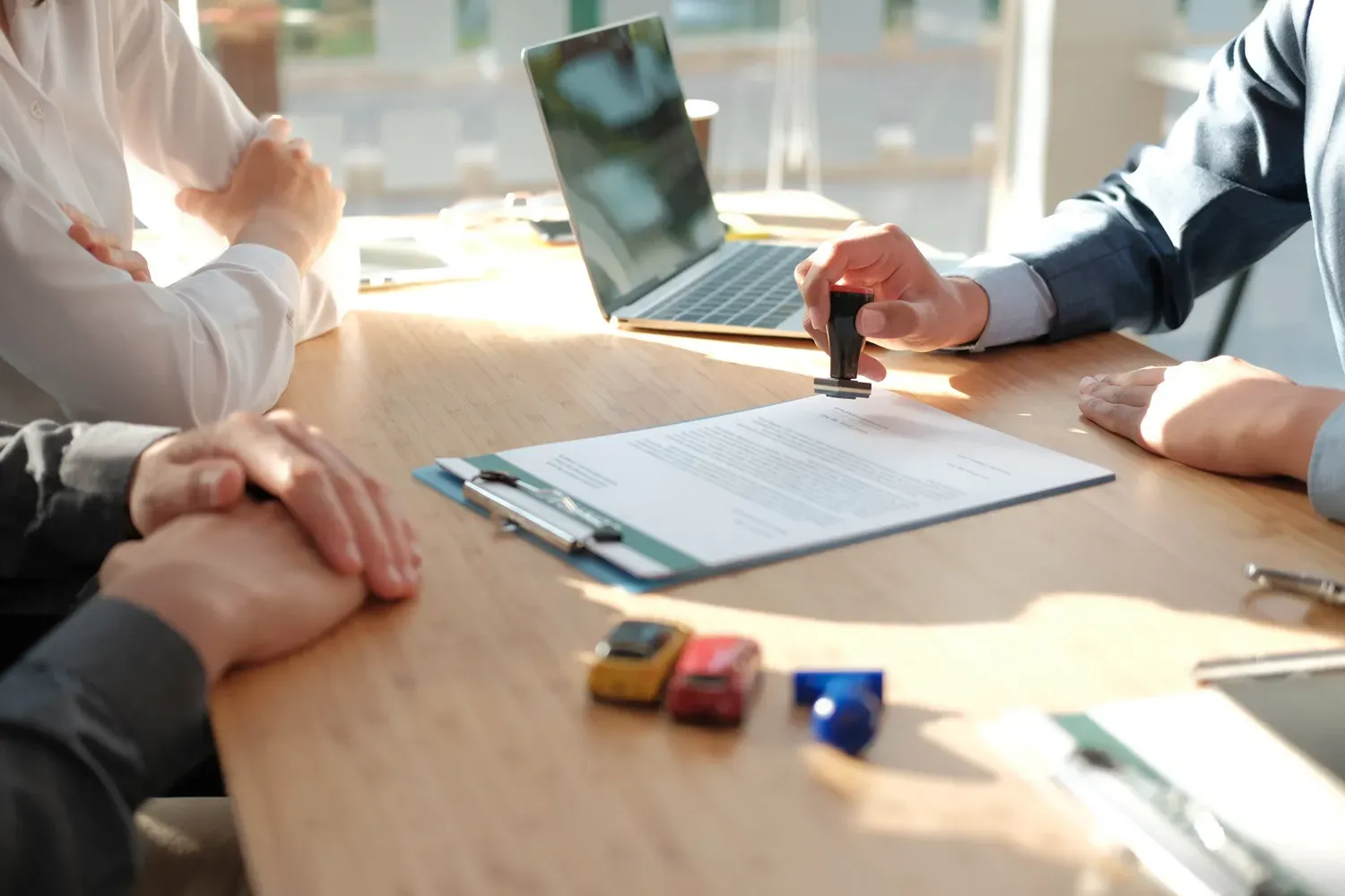 Close-up of a loan officer stamping approval on financial documents with toy cars and a laptop on the table, representing how to get a low-interest personal loan.