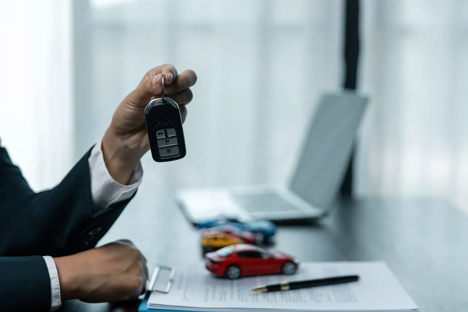 Person holding car keys over loan documents and toy cars on a desk, representing strategies to pay off a car loan faster and achieve financial freedom.
