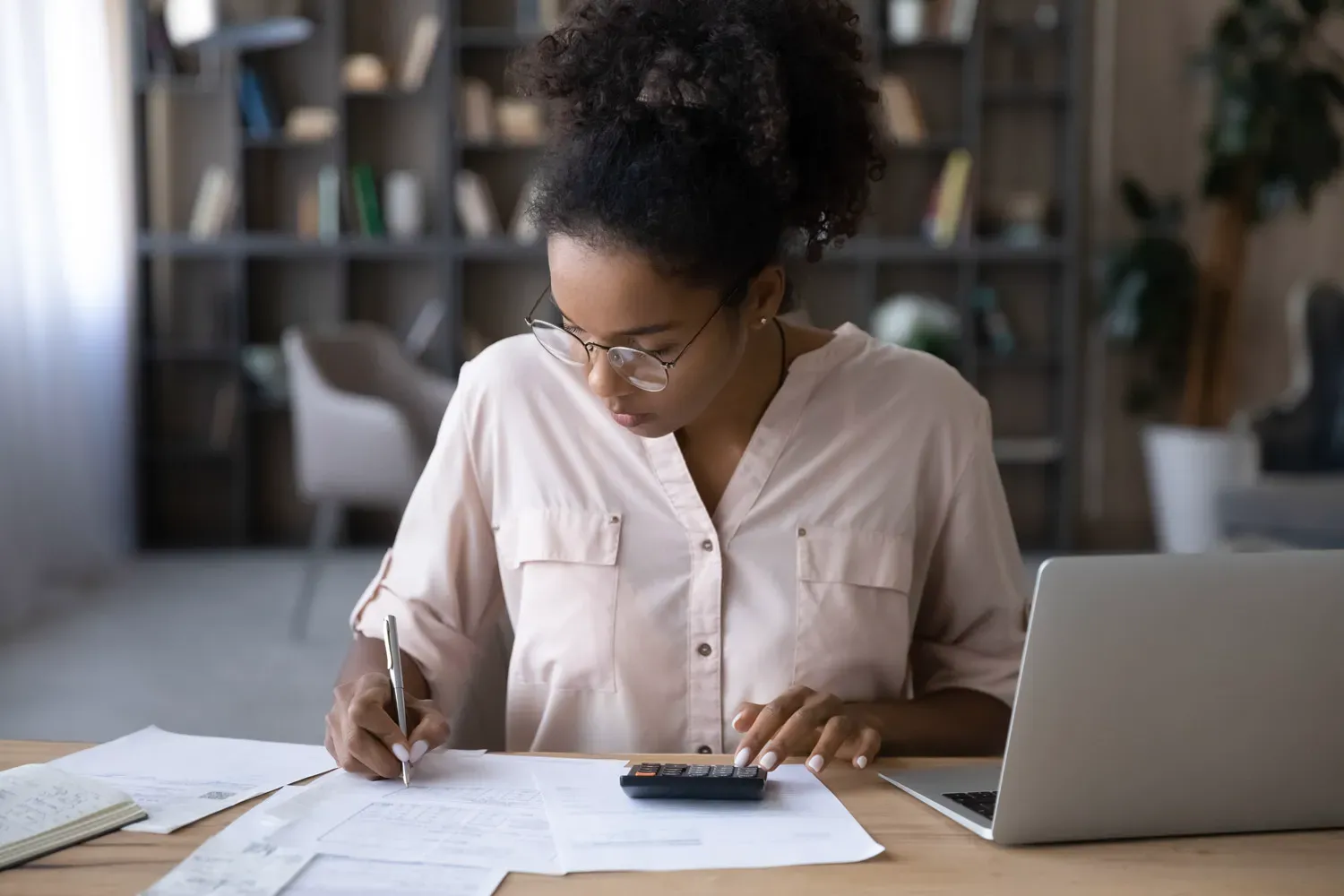 Woman reviewing financial documents with a calculator and laptop, illustrating the four main components of a personal budget: income, expenses, savings, and debt repayment.