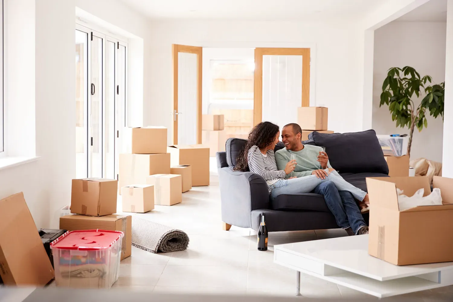 Happy couple sitting on a couch surrounded by moving boxes in their new home, symbolizing the excitement of homeownership and understanding mortgage basics.
