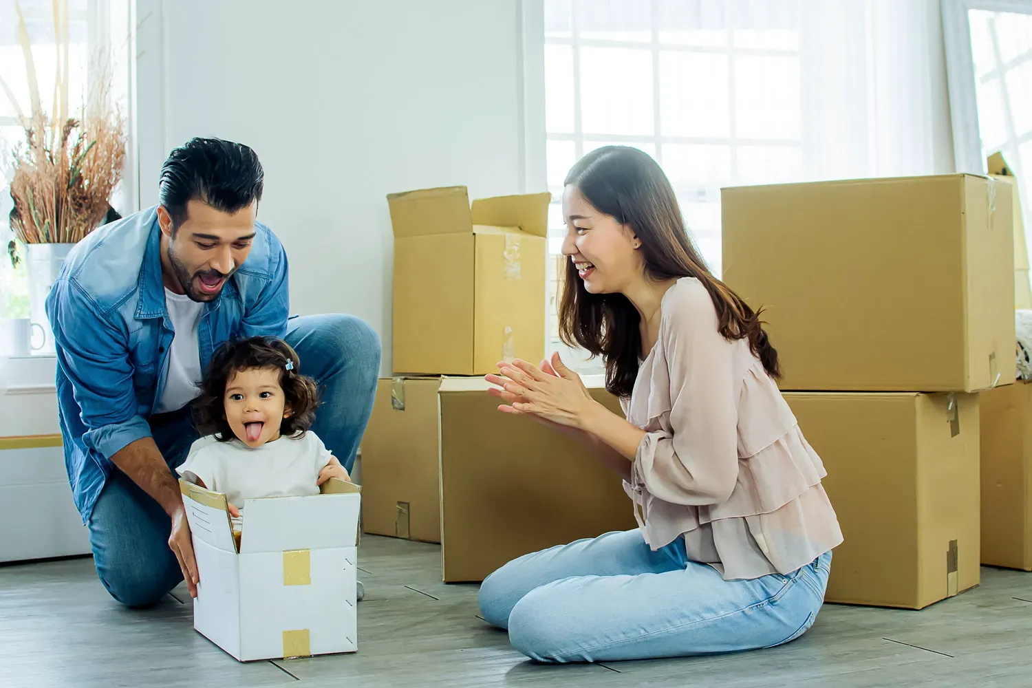Happy family playing with their young child among moving boxes in a new home, representing the excitement of planning and saving for a down payment on a house.