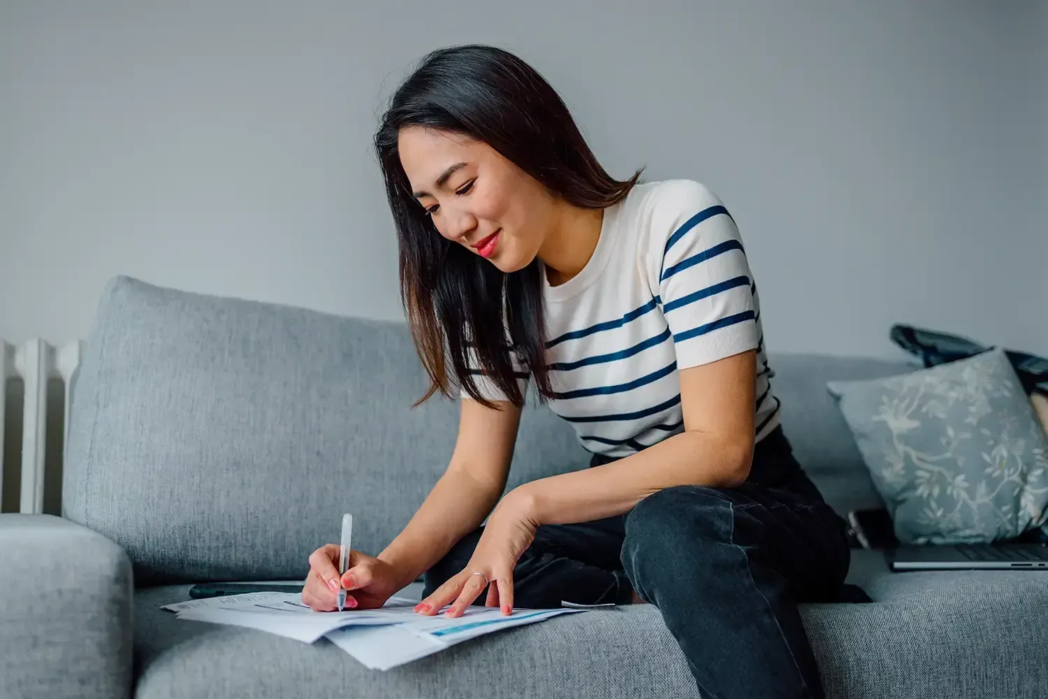 Woman sitting on a couch reviewing paperwork and taking notes about the pros and cons of using credit cards.