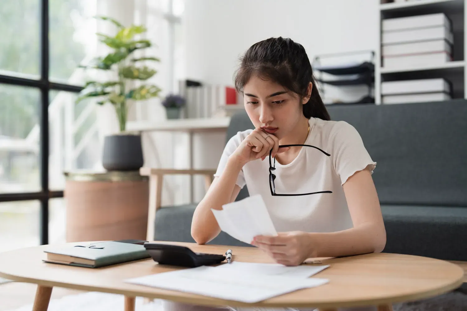 Woman sitting at a table reviewing bills and financial papers with a calculator nearby, representing the process of improving and repairing a credit score in five steps.