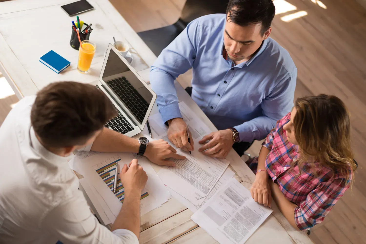 Overhead view of a couple meeting with a financial advisor, reviewing documents and charts together — representing a discussion about whether to open a joint checking account.