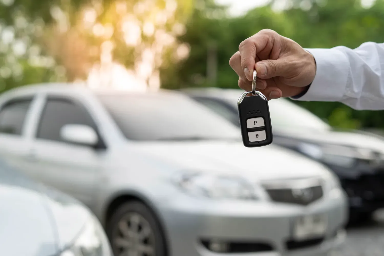 Person holding a car key in front of parked vehicles, representing the decision between leasing or buying a car.