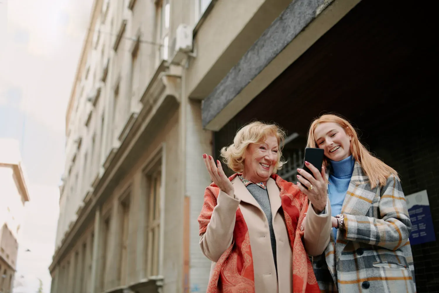 Older and younger women smiling while looking at a smartphone, symbolizing how future Social Security changes will affect multiple generations.