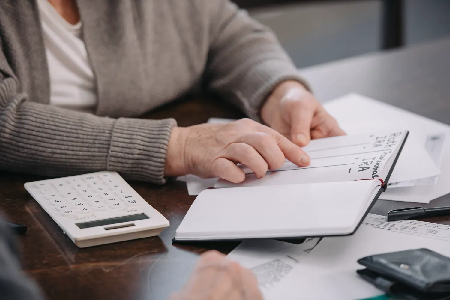 Person reviewing notes comparing Roth and Traditional IRAs while planning for retirement, with papers and a calculator on the table.