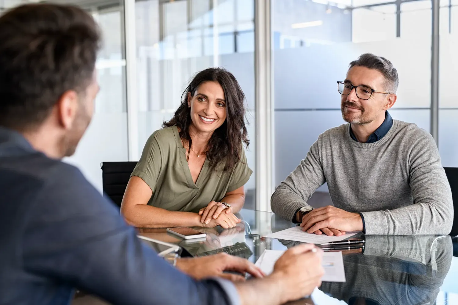 Smiling couple meeting with a financial advisor in a modern office, representing the personalized and member-focused service credit unions offer compared to traditional banks.