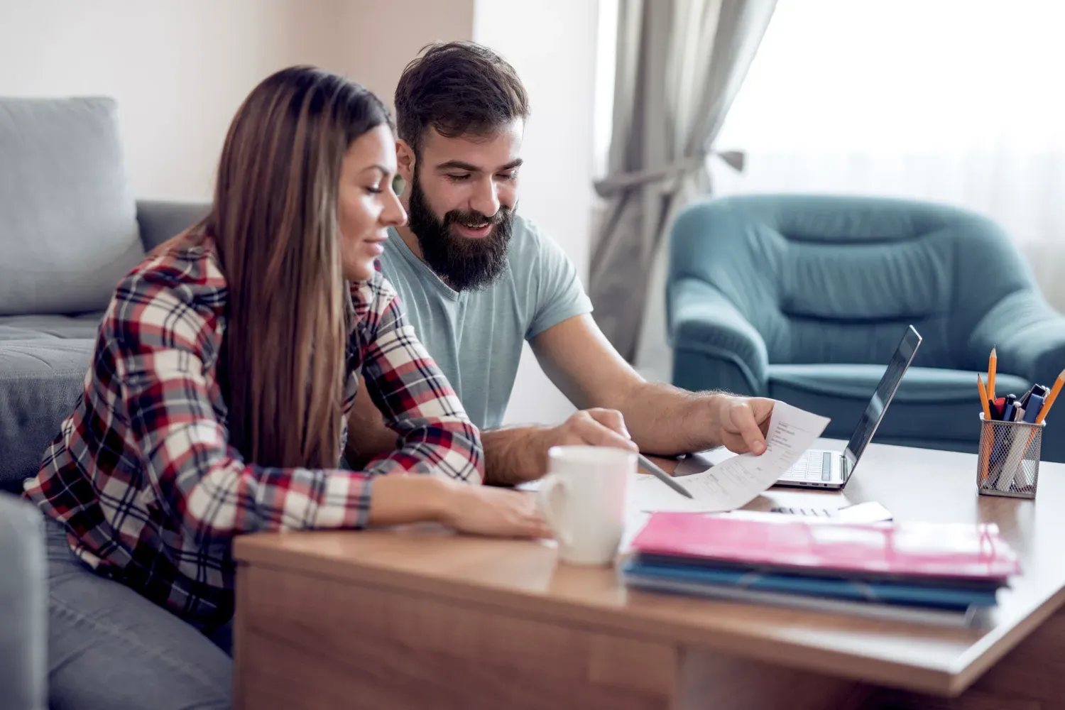 Couple reviewing financial documents together at home with a laptop and coffee mug, representing a comprehensive guide to using a personal loan wisely.